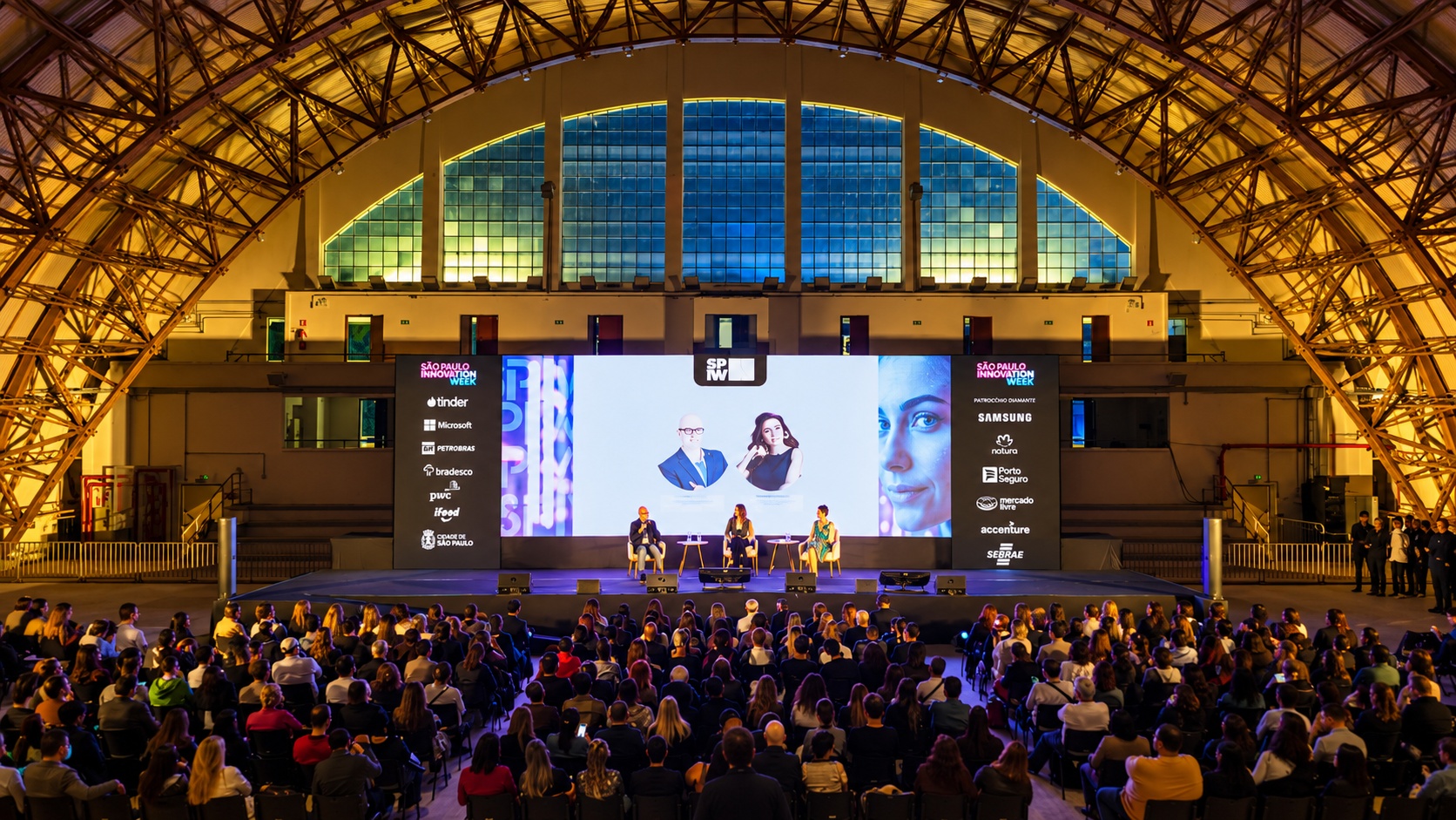 Conferência do SPIW com público, palco e barra de patrocinadores